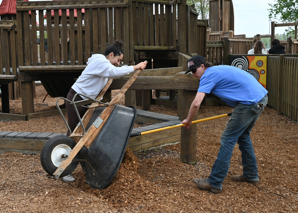a girl dumping a wheelbarrow and boy raking mulch out of the wheelbarrel