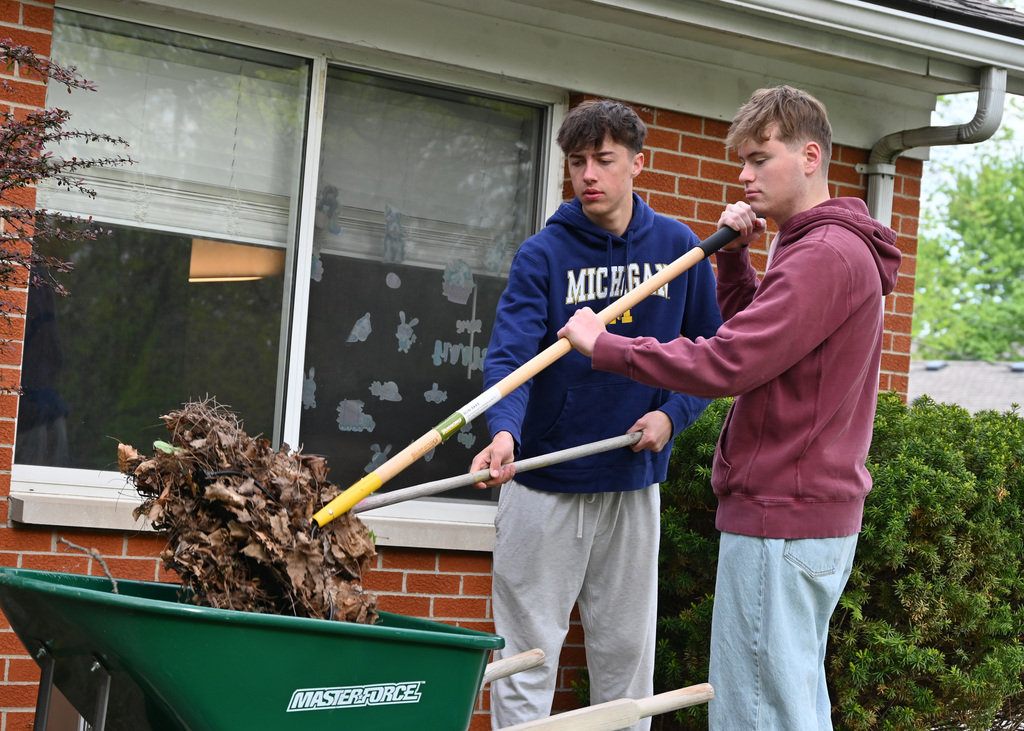 two boys filling a wheelbarrell with leaves