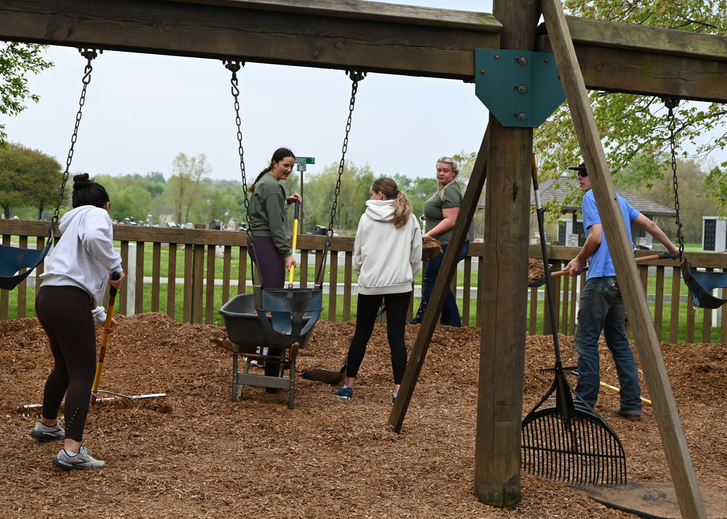 4 people spreading mulch with rakes at a playground