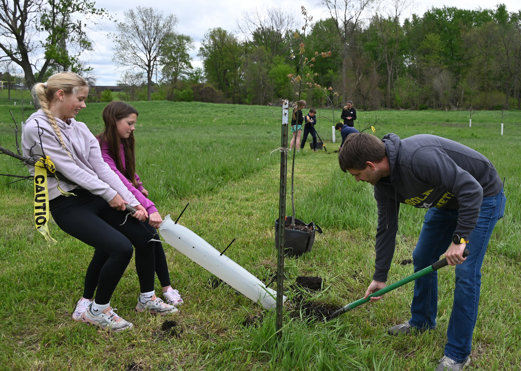 Two students and teacher digging up a tree 