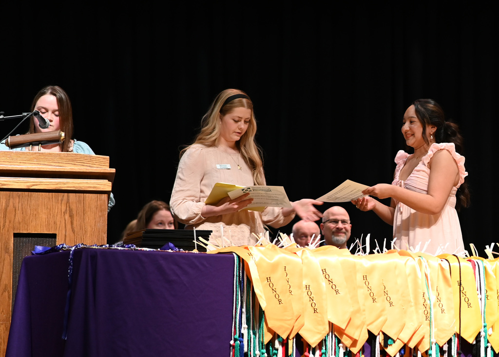 girl recieved certificate by another girl, woman at podium microphone