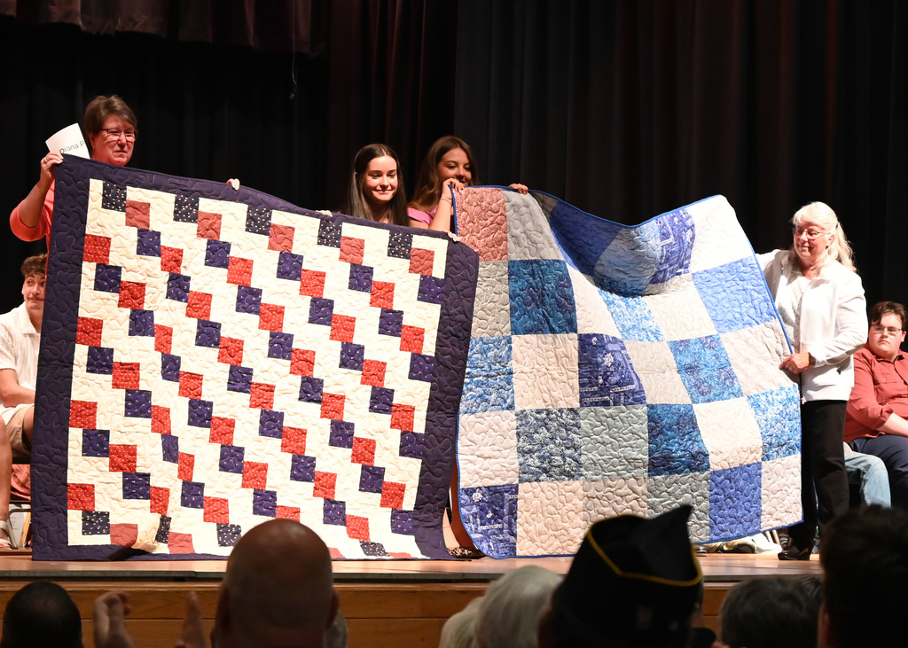 two woman and two girls hold up quilts