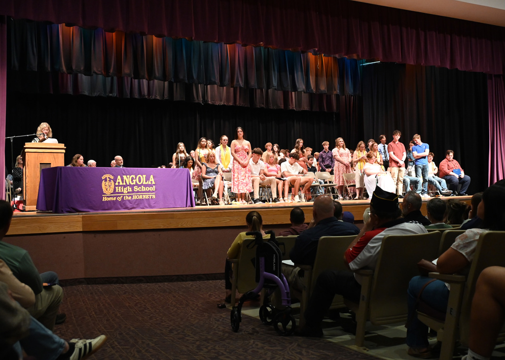 A stage with students sitting in chairs and standing by chairs at Angola high School