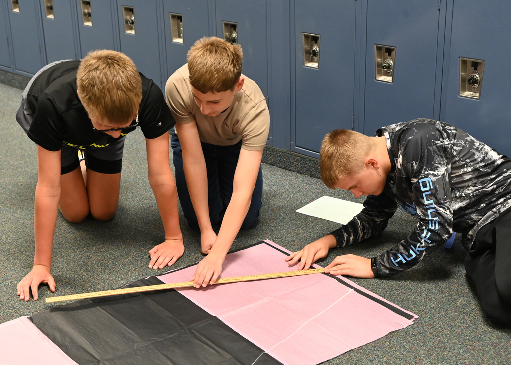 three boys measuring long sheets of paper