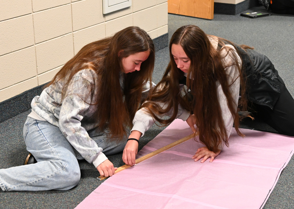 two girls measuring long sheets of paper