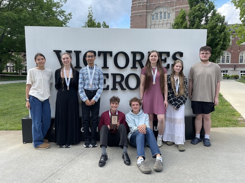 8 high school students 6 standing 2 sitting in front of sign at Purdue University