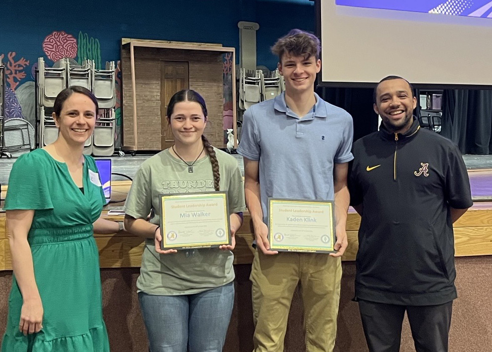 two student hold awards with a teacher on each side