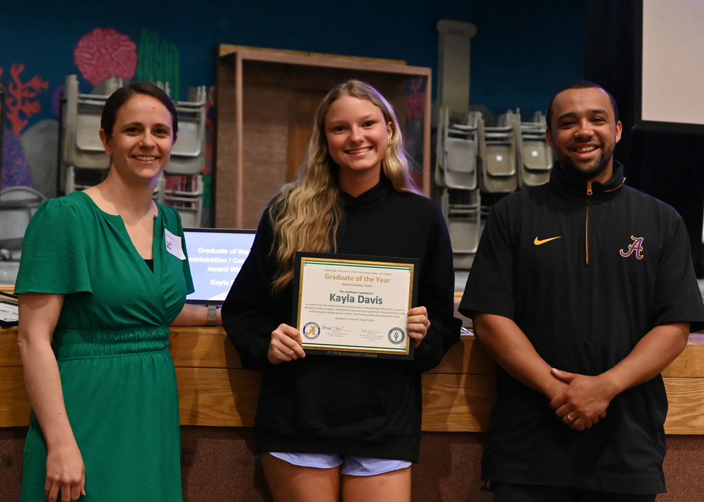 student hold awards with a teacher on each side