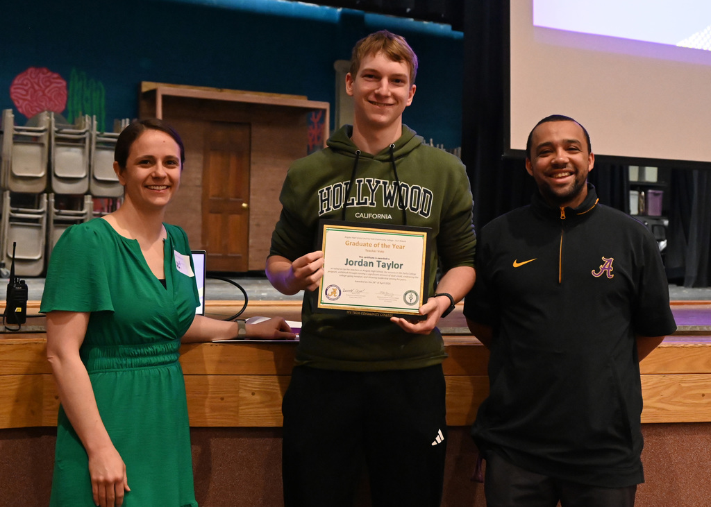 student hold awards with a teacher on each side