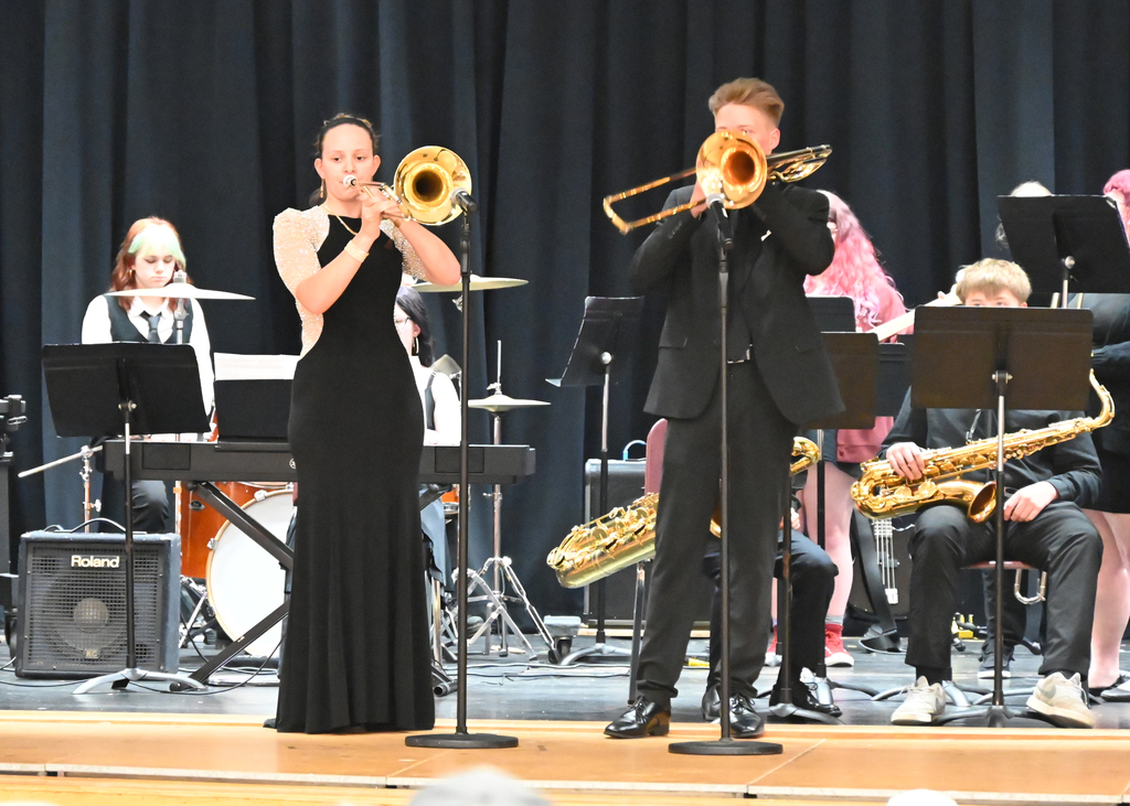 a teen girl and a teen boy playing trombone on a stage