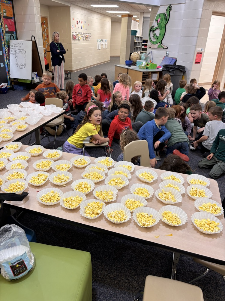 Classroom of kids sitting behind tables of popcorn