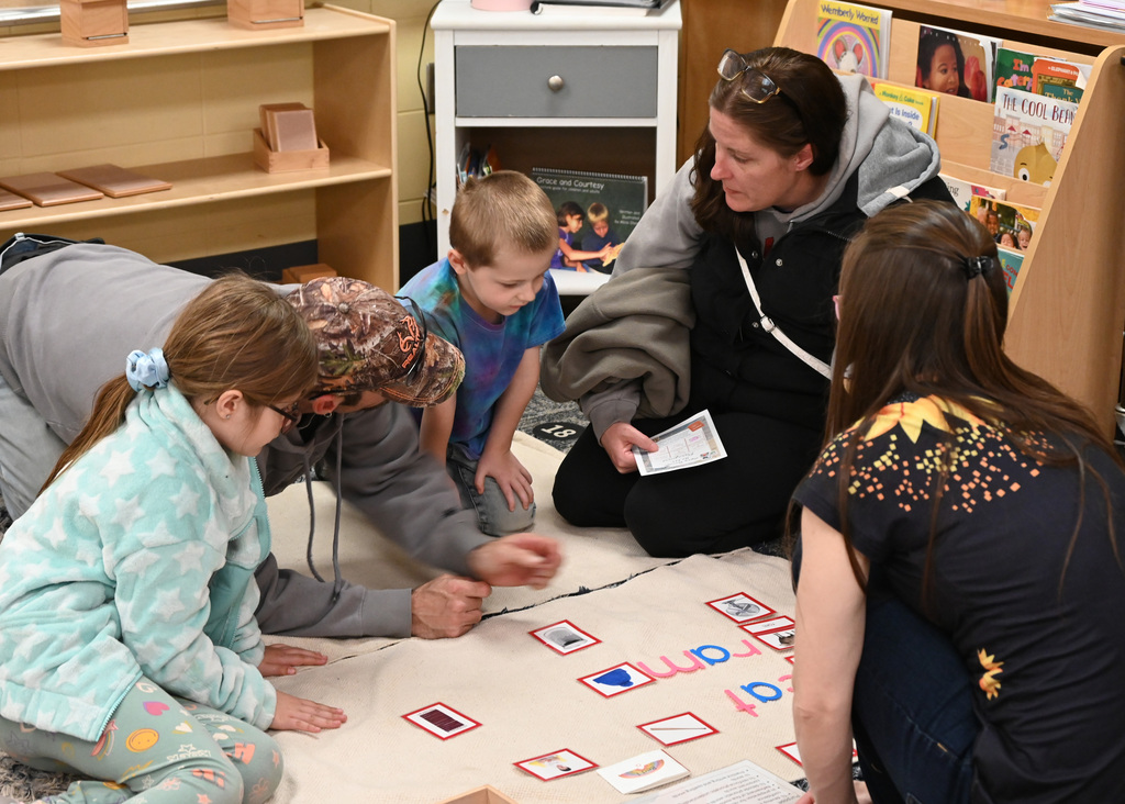 two adults and 3 chilren sitting on floor around a word game
