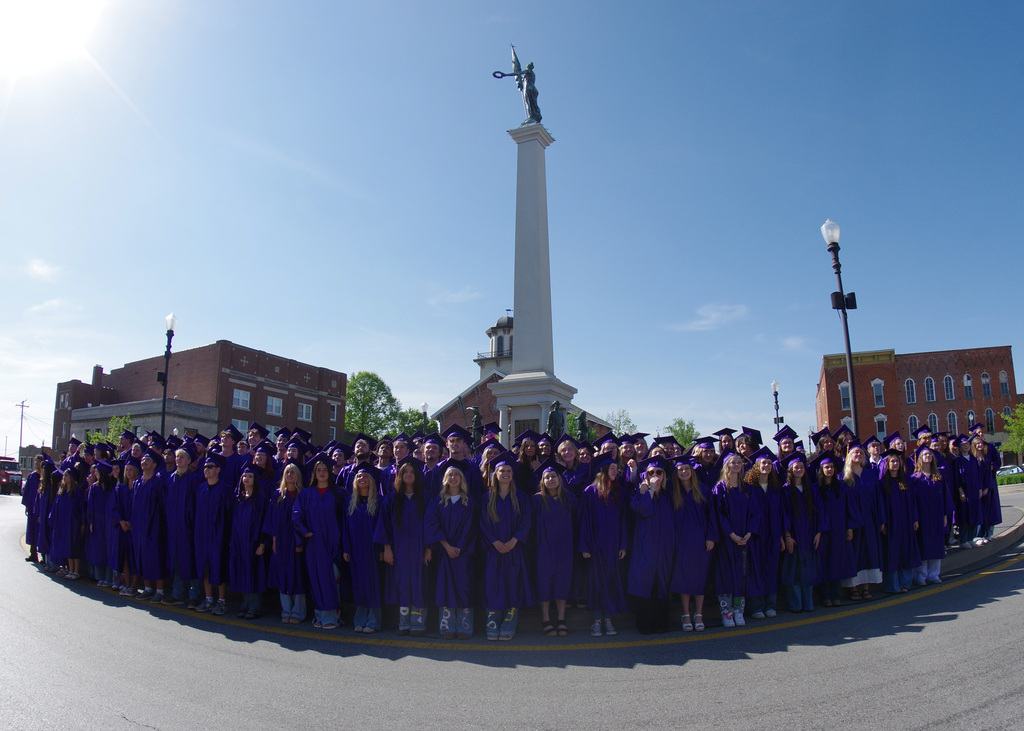 very large group of students in caps and gowns standing in front of monument