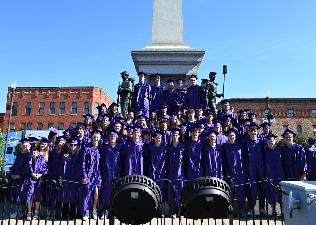 very large group of students in caps and gowns standing in front of monument