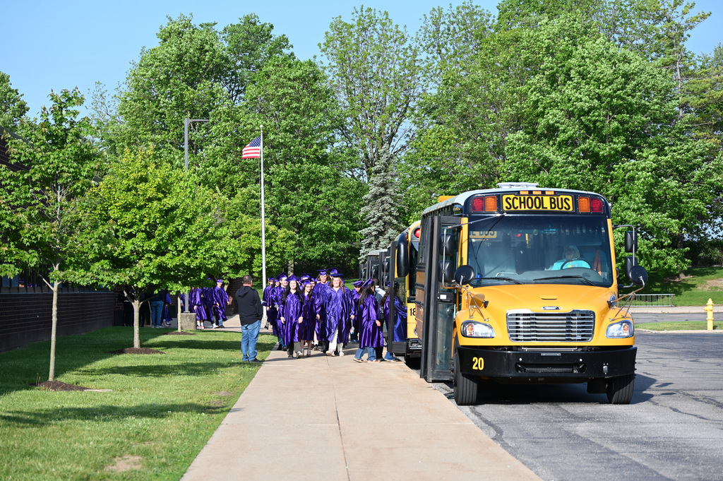 Students in purple caps and gowns getting onto busses