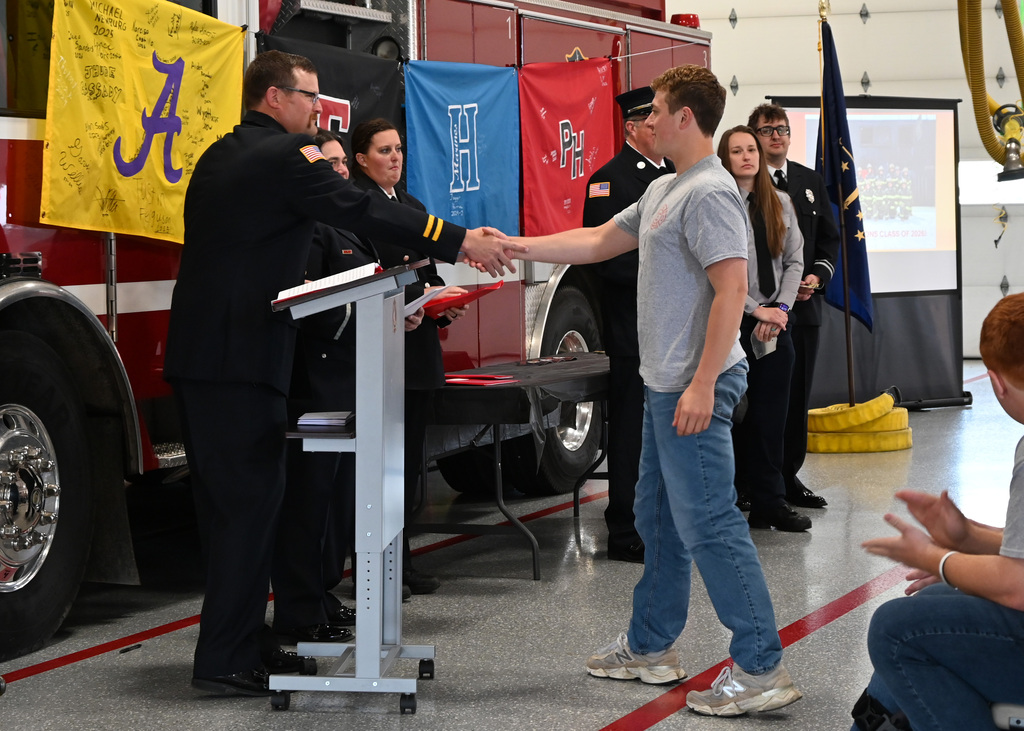 a line of Fire fighters in dress uniform shaking hands with a boy