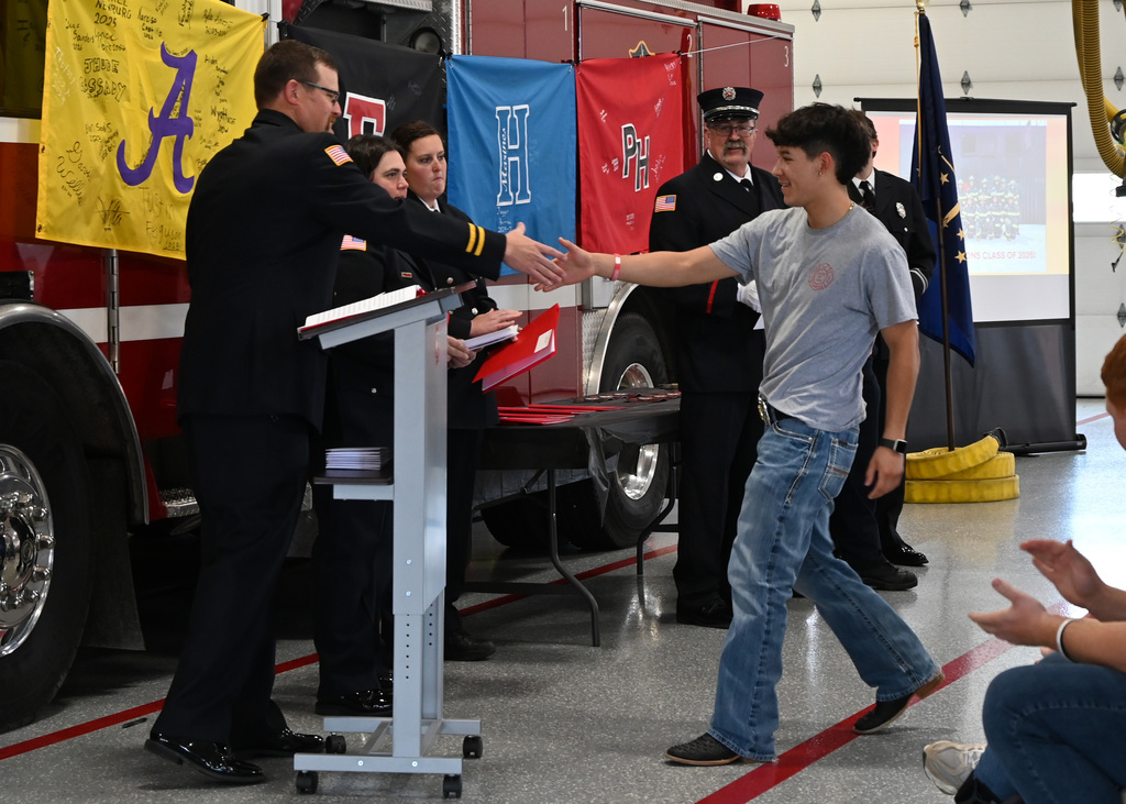 a line of Fire fighters in dress uniform shaking hands with a boy