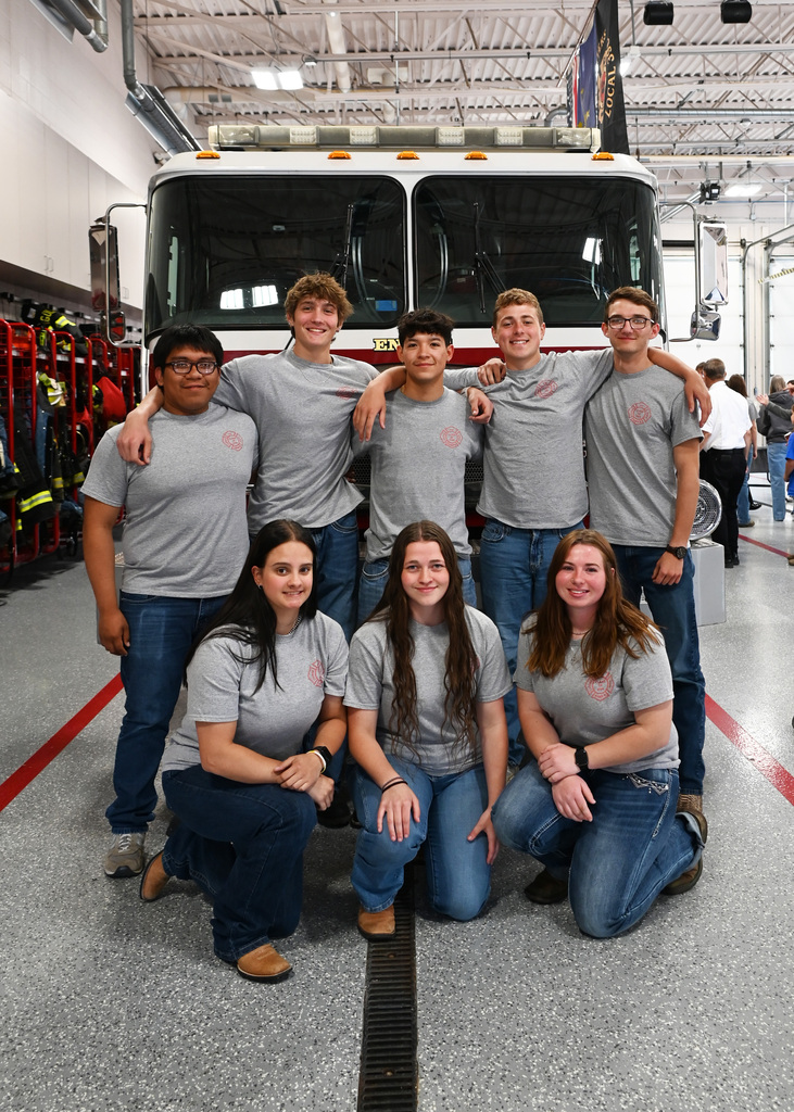 8 seniors in high school all in matching gray shirts in front of fire truck, 5 boys standing in bakc 3 girls kneeling in front