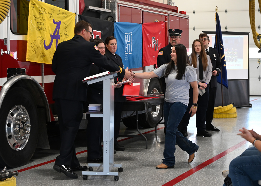a line of Fire fighters in dress uniform shaking hands with a girl