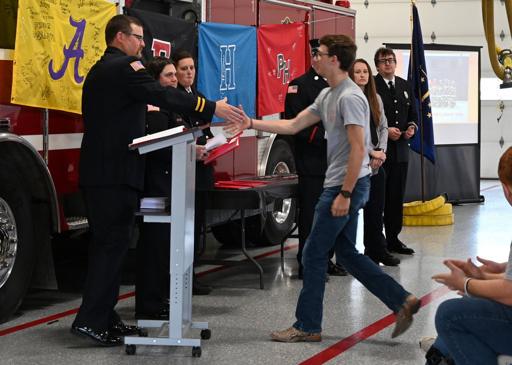 a line of Fire fighters in dress uniform shaking hands with a boy
