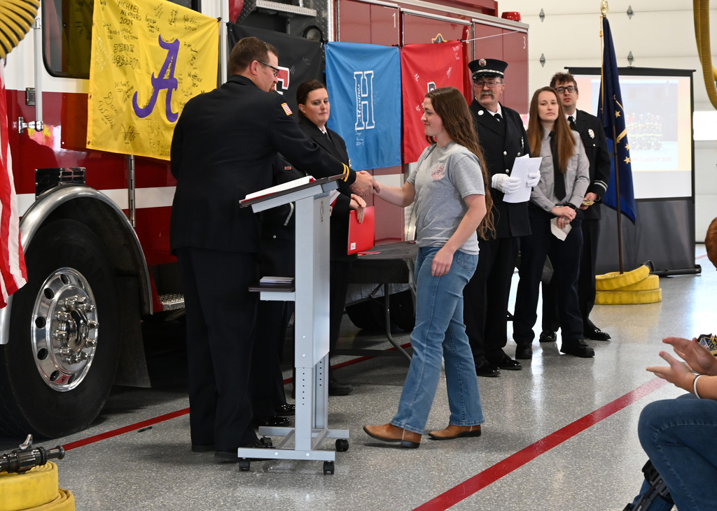 a line of Fire fighters in dress uniform shaking hands with a girl