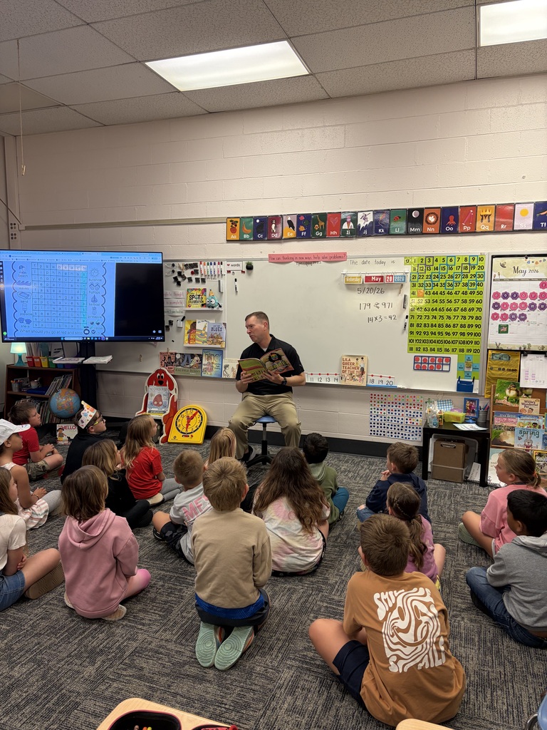 Man sitting in front of class of kids sitting cross legged on floor as he reads them a story