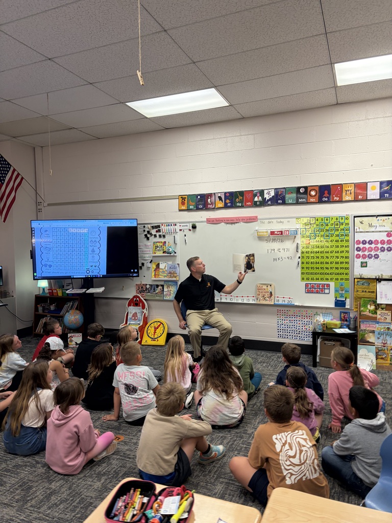 Man sitting in front of class of kids sitting cross legged on floor as he reads them a story