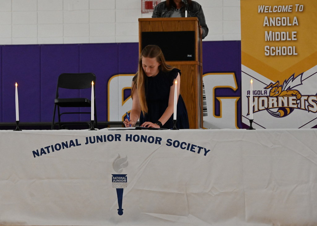 Girl at a table with National Junior Honor Society signing a book