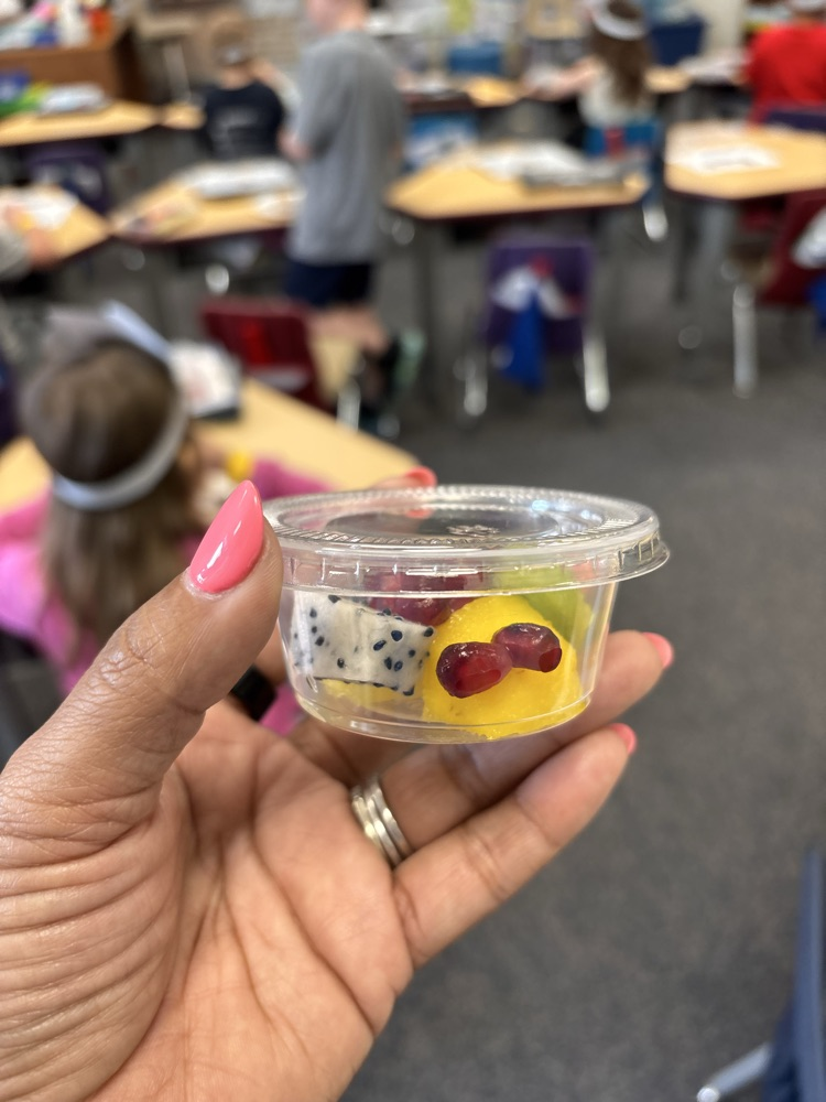 a hand holding cup with pineapple, pomegranate, kiwi