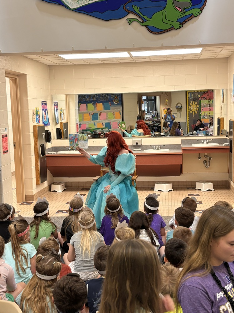 a person dressed as Disney Princess Ariel reading to a class of children sitting on floor