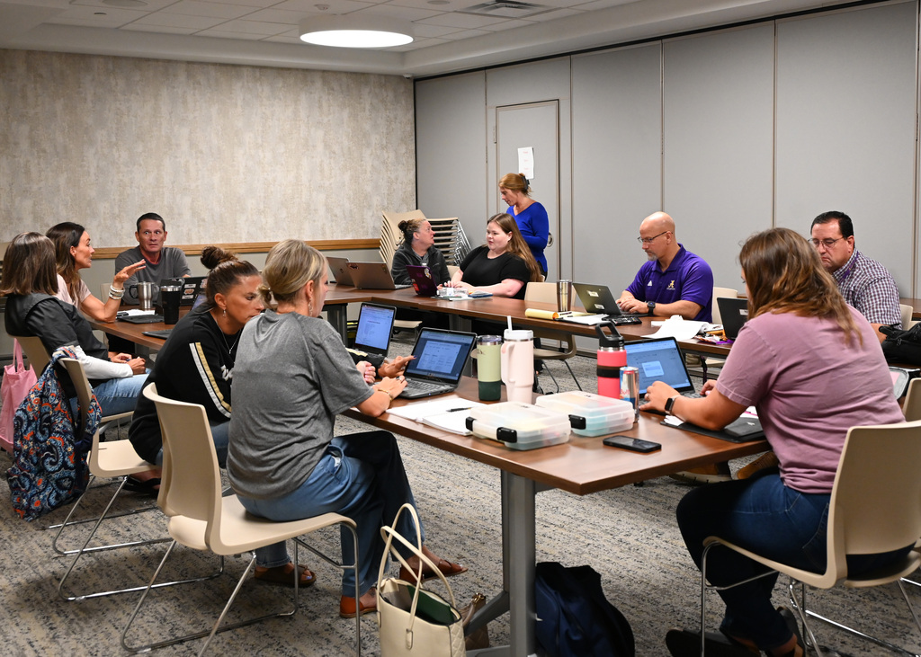 9 adult sitting and working on labtops at a square table