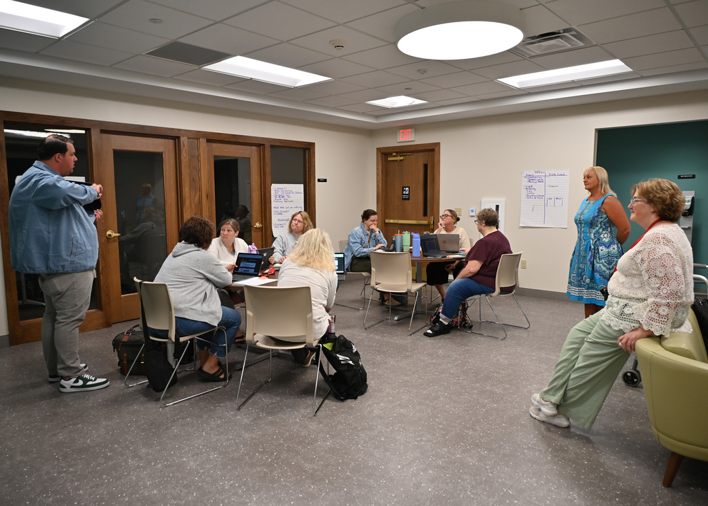 adults in a room some around 2 table 3 standing around those having a discussion