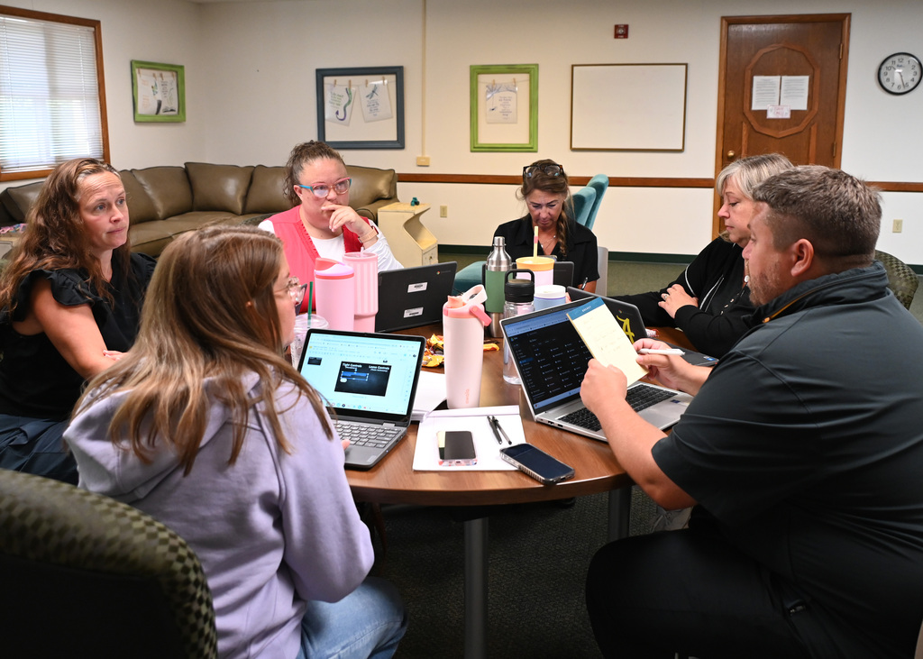 six people sitting around a table, with laptops working together.