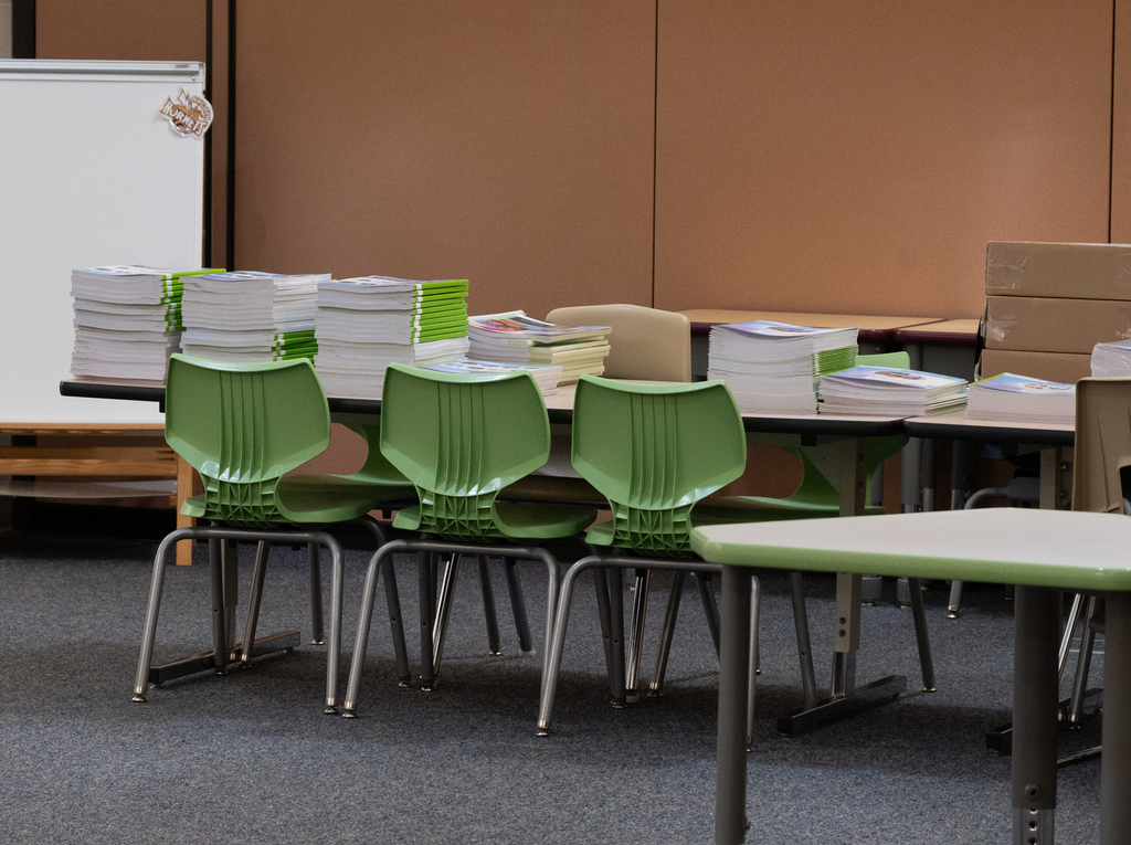 a student table with books stacked on it and green chairs around it