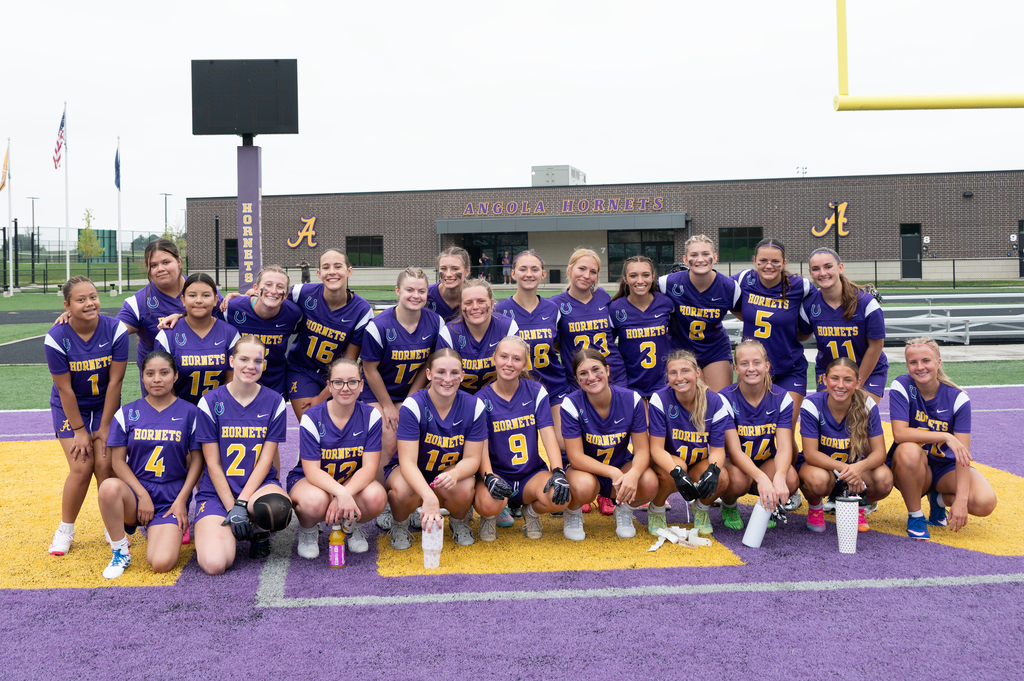 Girls AHS flag football team lined up together in front of Angola hornets building
