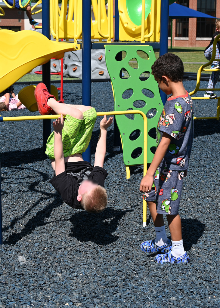 boy hanging from bar in playground while other student watches