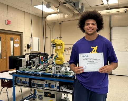 Young man standing next to manufacturing equipment holding a certificate