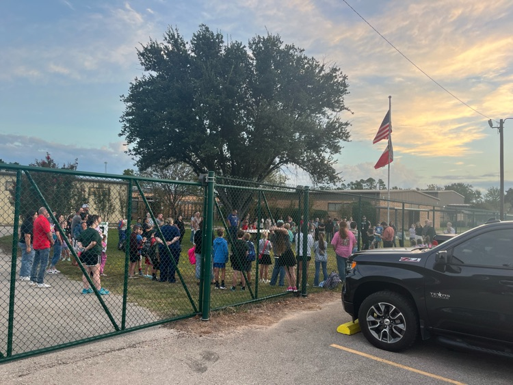 Group of students and adults gathered around the school flag pole.