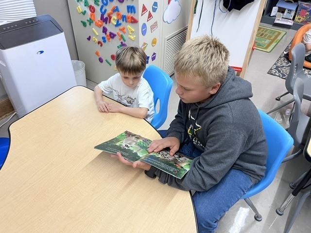 An older student is reading to a younger student