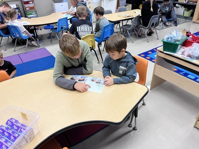 An older student is reading to a younger student
