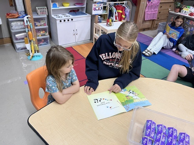 An older student is reading to a younger student