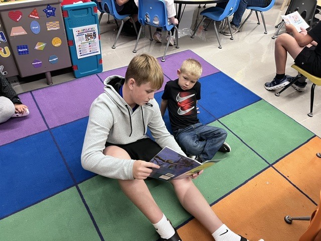 An older student is reading to a younger student