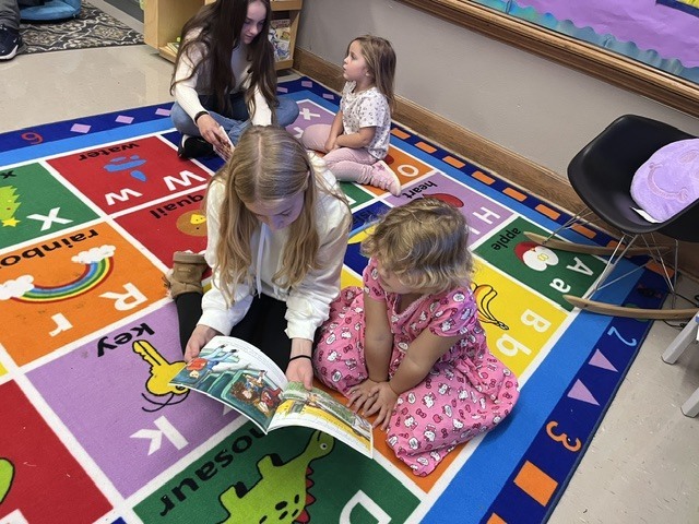 An older student is reading to a younger student