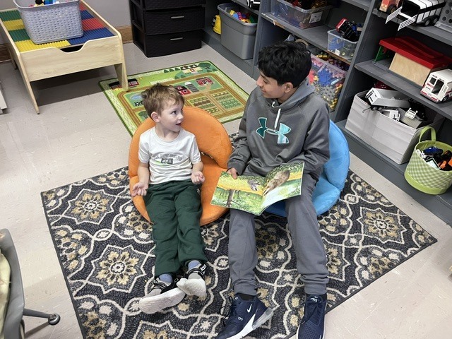 An older student is reading to a younger student