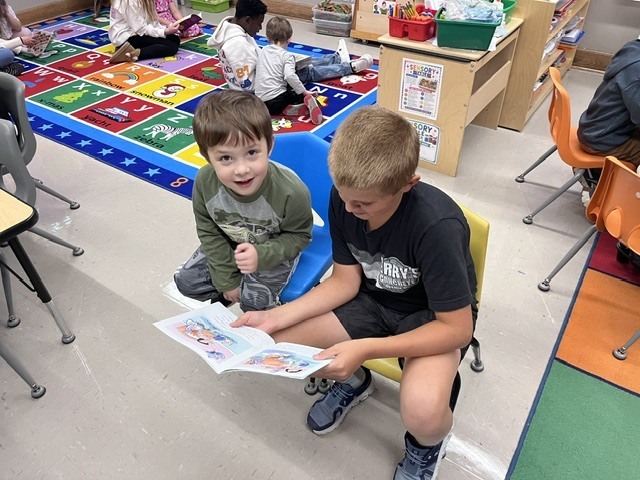 An older student is reading to a younger student