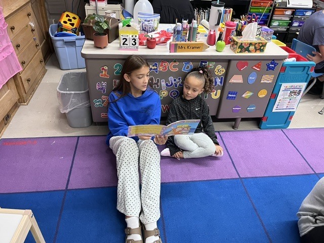 An older student is reading to a younger student