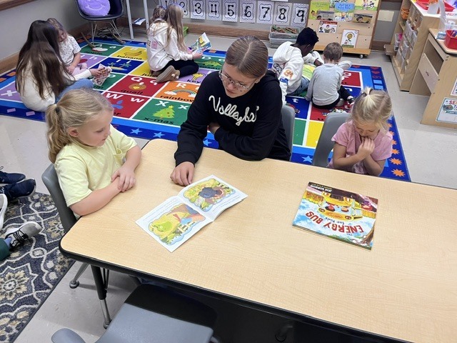 An older student is reading to younger students