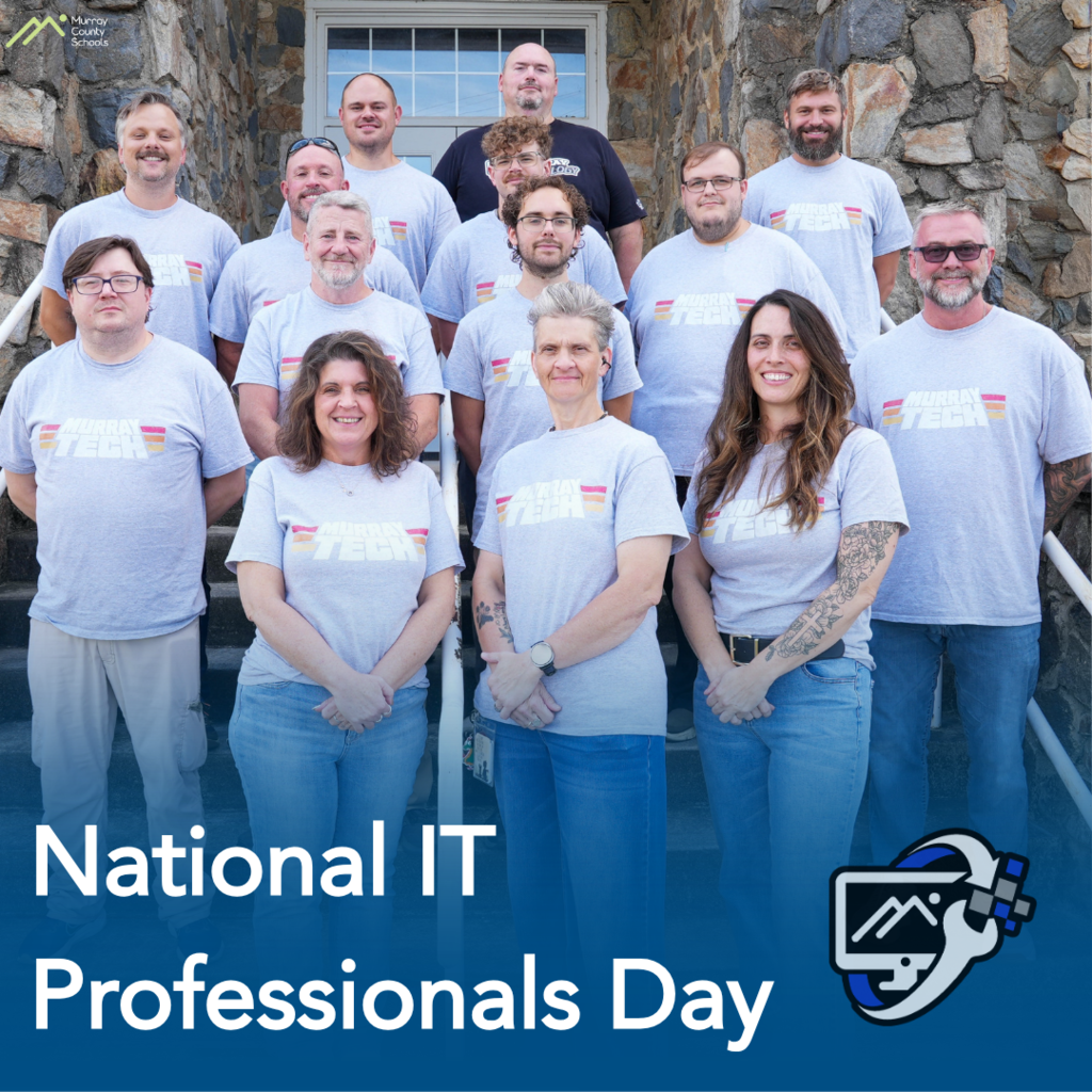 Group of individuals in matching shirts standing outdoors, in front of a stone wall, smiling for a picture.