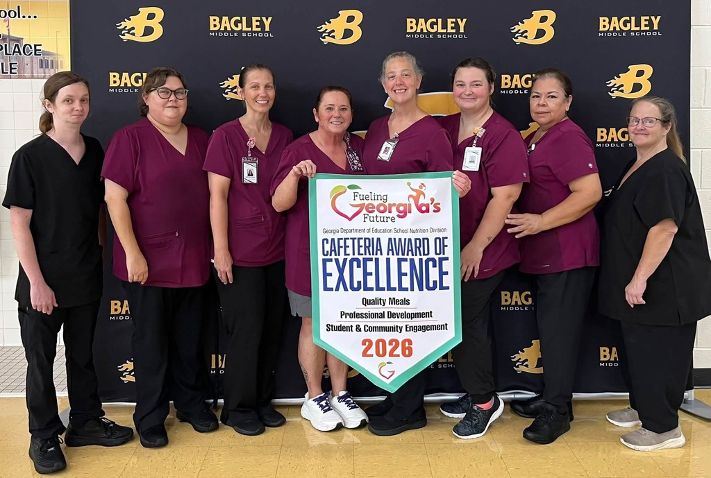 A group of nine individuals in purple uniforms pose behind a sign saying "Cafeteria Award of Excellence 2026."