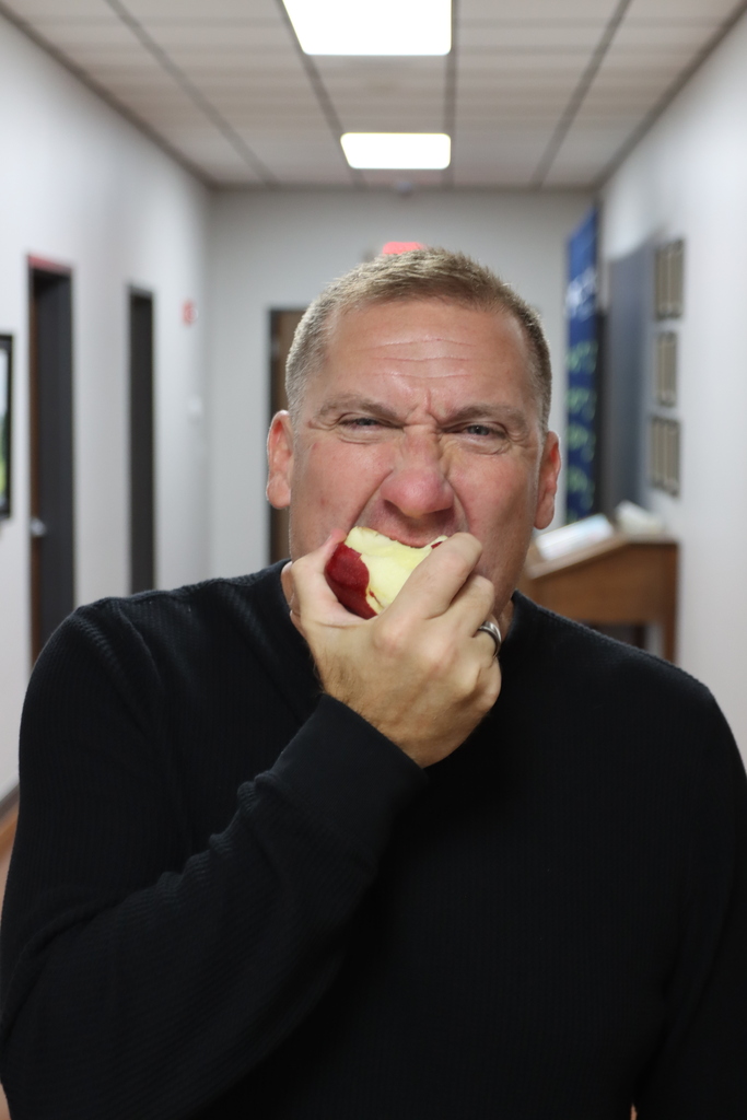 A man wearing a black long-sleeve shirt eats a piece of apple in a hallway.